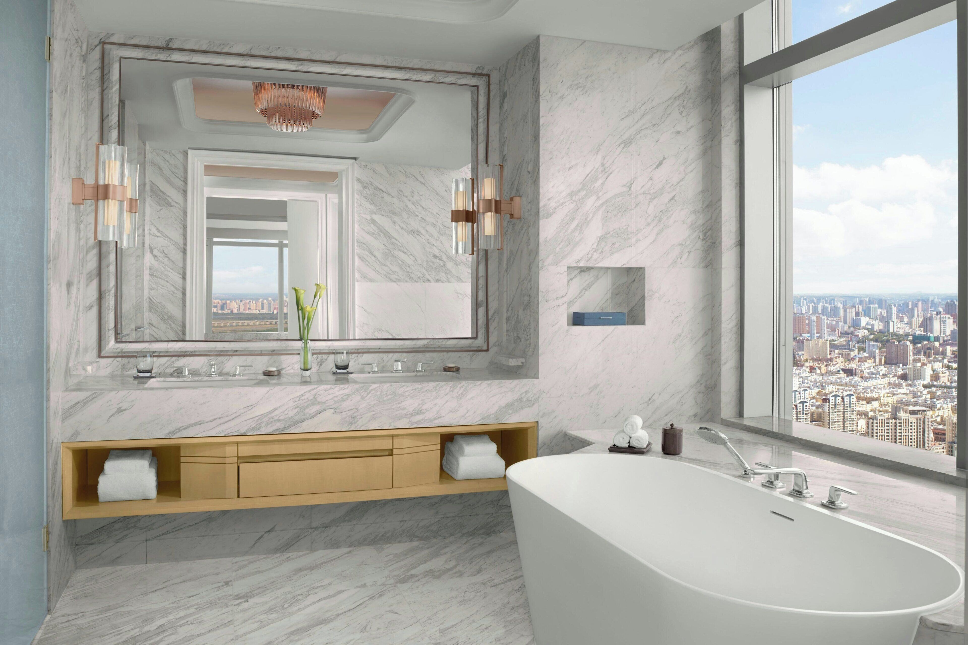 A modern bathroom with a freestanding bathtub, a large mirror, and a city view.