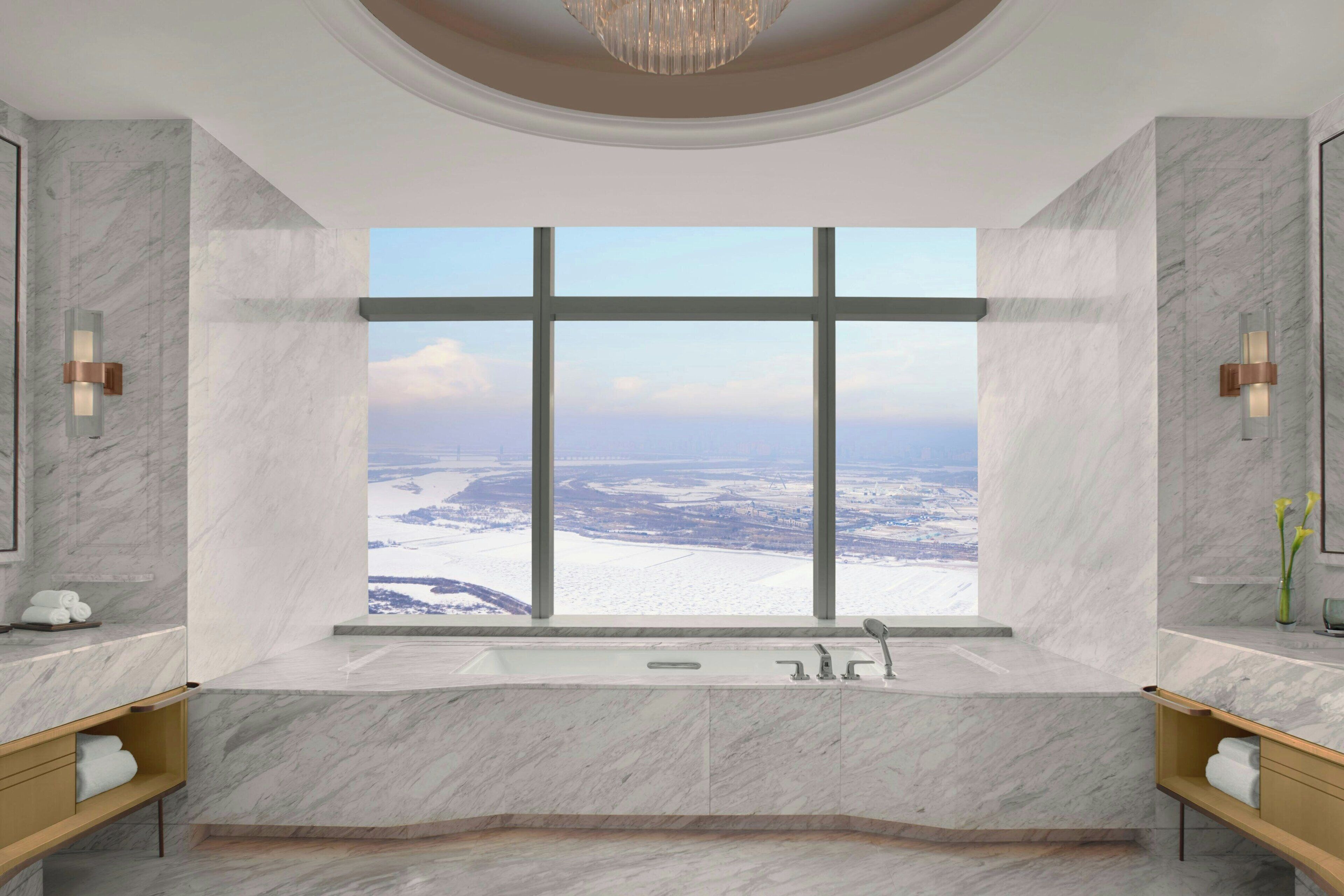 A modern bathroom with a large window, marble walls, and a bathtub.