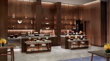 A modern hotel lobby with wooden paneling, a central reception desk, and a buffet area with various food items and decorative objects.