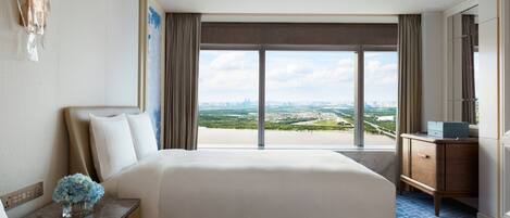A hotel room with two beds, a nightstand with a vase of flowers, a dresser, and a large window offering a city view.
