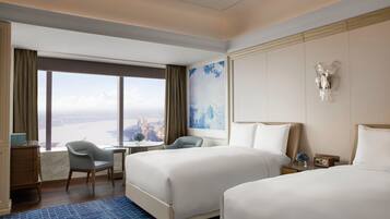 Habitación de hotel con dos camas, un escritorio, una silla y vistas a un paisaje urbano.