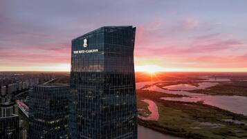 A high-rise building with "THE RITZ-CARLTON" signage, surrounded by a cityscape and a river at sunset.