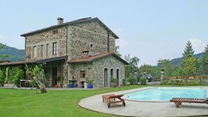 Una casa de piedra con piscina, rodeada de un césped cuidado y un paisaje montañoso.