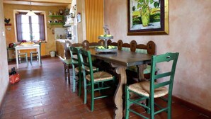 Un área de comedor con una mesa de madera y sillas verdes, una cocina al fondo y un cuadro en la pared.
