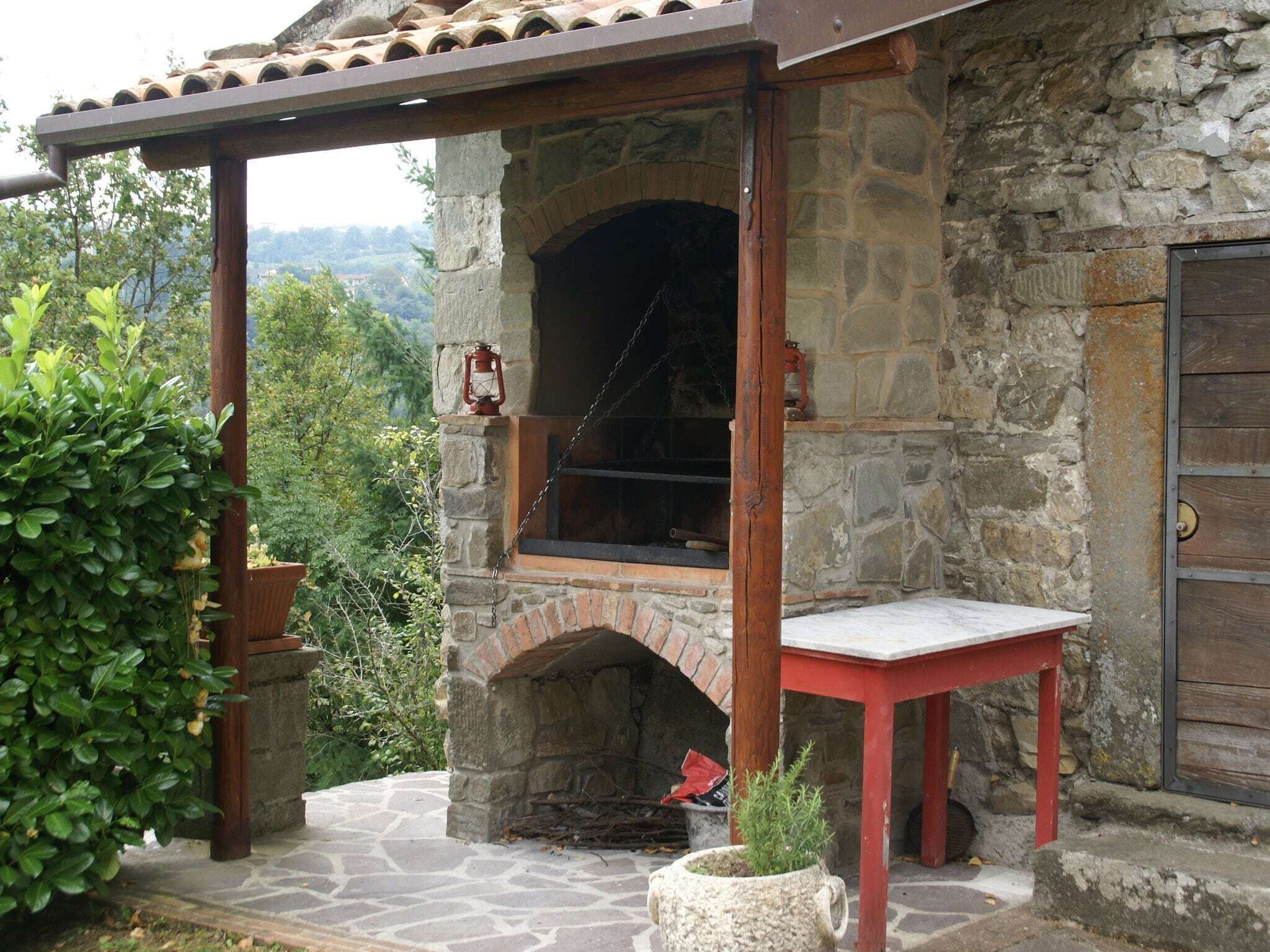 A stone building with a brick oven, a wooden pergola, and a red table.