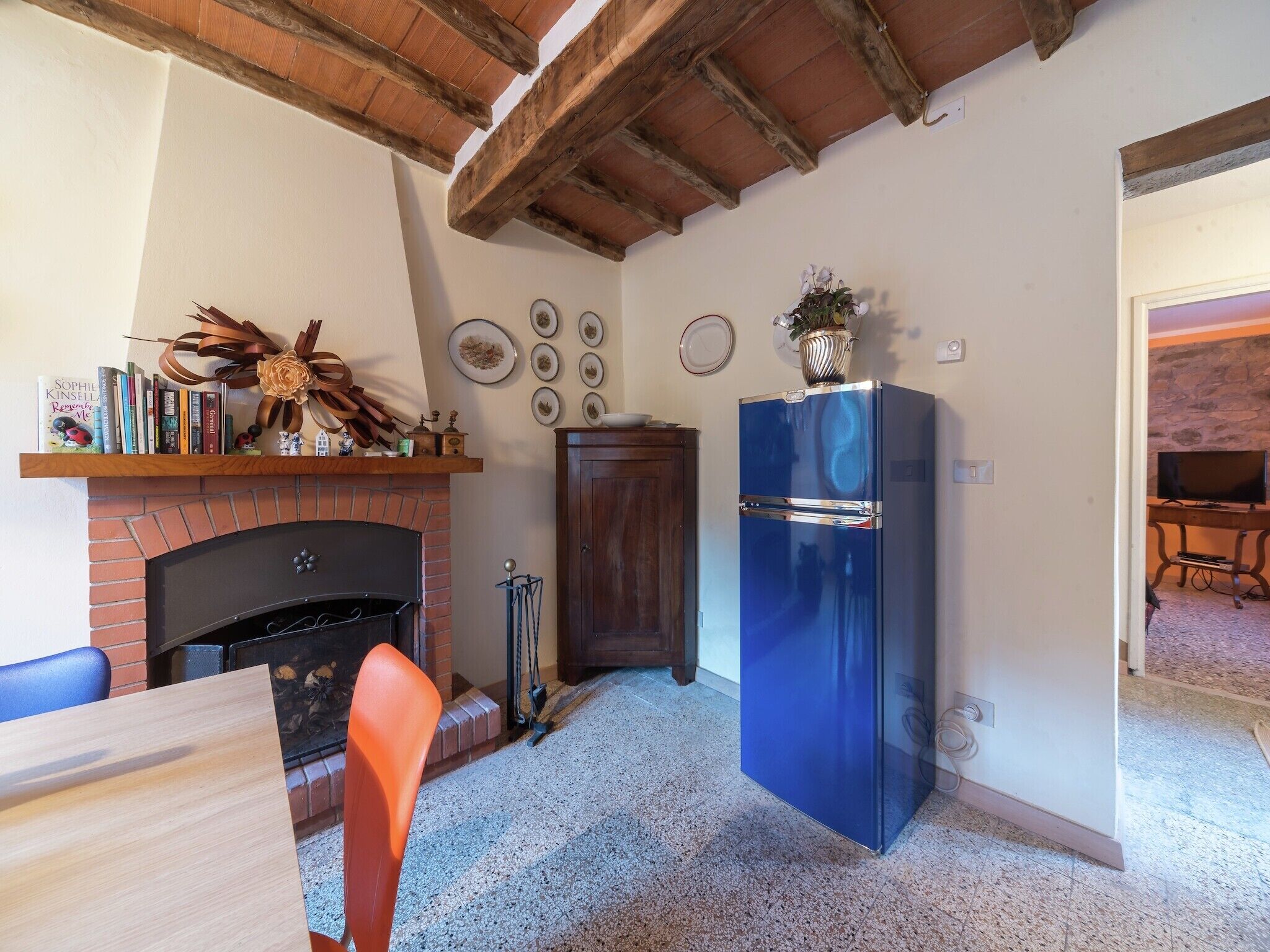 A cozy living room with a brick fireplace, a blue refrigerator, and a dining area with a table and chairs.