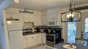 A kitchen with white cabinets, a refrigerator, a microwave, an oven, and a dining table with chairs. - King Suite on Canal (Saint James City)