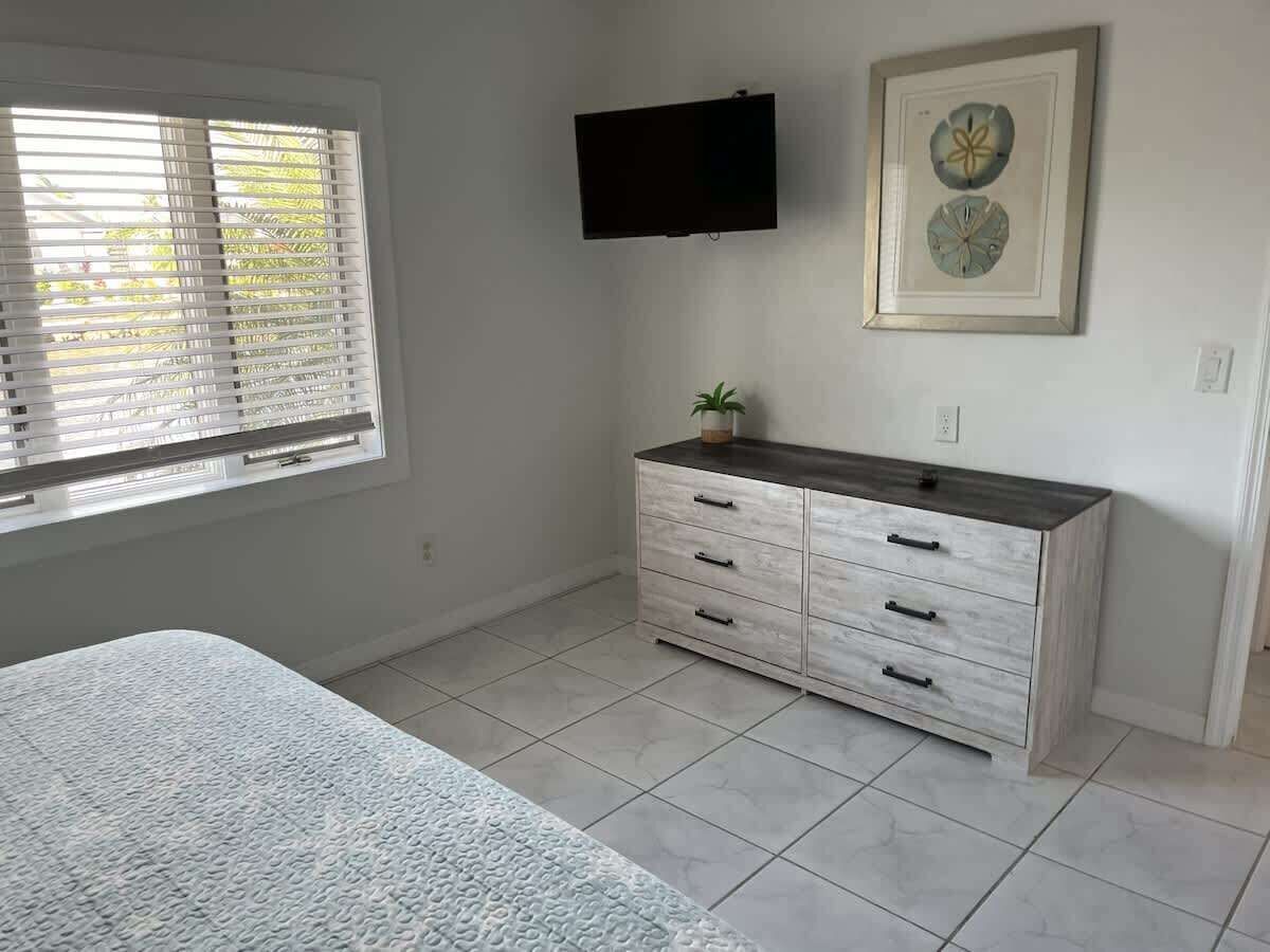Une chambre à coucher avec un lit, une commode, un téléviseur et une fenêtre avec des stores.