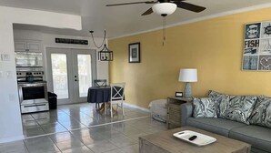 A living room with a sofa, a coffee table, a lamp, and a ceiling fan. There is a kitchen area with an oven and a dining table. - King Suite on Canal (Saint James City)