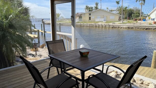A wooden deck with a table and chairs overlooking a body of water, palm trees, and a house in the background. - King Suite on Canal (Saint James City)