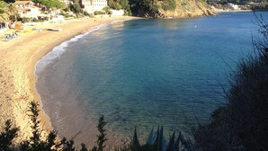 Una playa costera con agua cristalina, orilla arenosa y edificios al fondo.