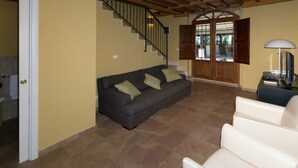 A living room with a dark grey sofa, a white armchair, a wooden staircase, and a wooden door leading outside.