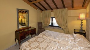 A bedroom with a large bed, a wooden dresser, a chair, a window with curtains, and a lamp.