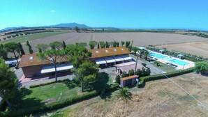 A building with a tiled roof, a swimming pool, and a landscaped area with trees and a view of the countryside.