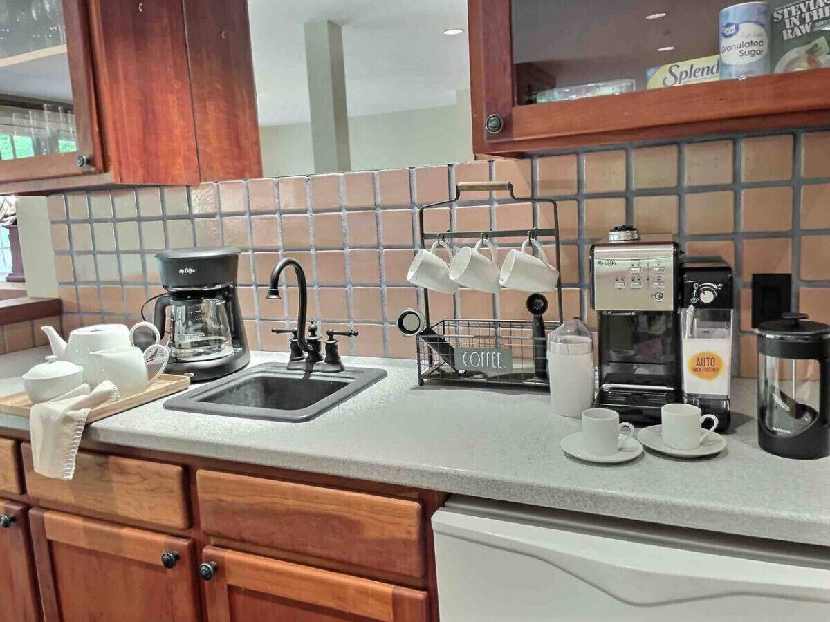 Una cocina con estación de café, que incluye cafetera, tazas y hervidor.
