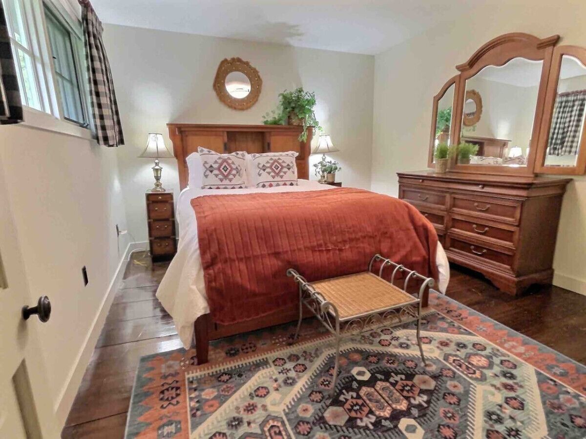 A bedroom with a bed, a nightstand, a dresser, a mirror, and a patterned rug.