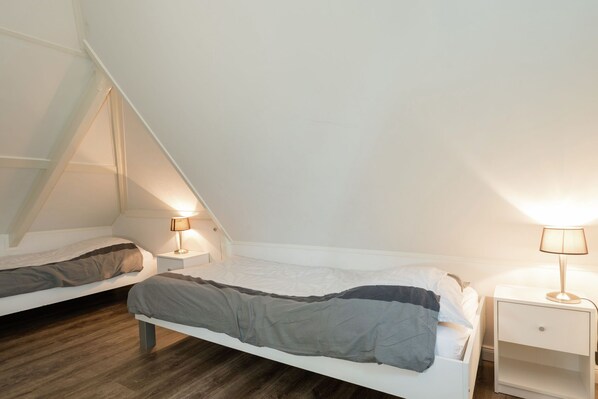 A bedroom with two beds, each with a nightstand and a lamp. The room has sloped ceilings and wooden flooring. - Elegant Apartment in Hoorn with Roof Terrace (Hoorn)