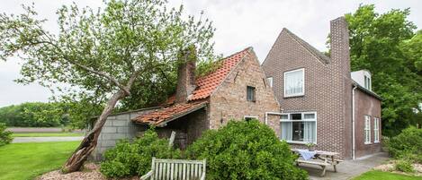 A brick house with a sloped roof, a wooden bench, and a small garden area.
