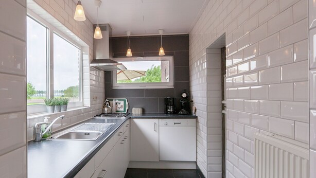 Una cucina compatta con mobili bianchi, un piano di lavoro nero, una finestra con vista e illuminazione a sospensione.