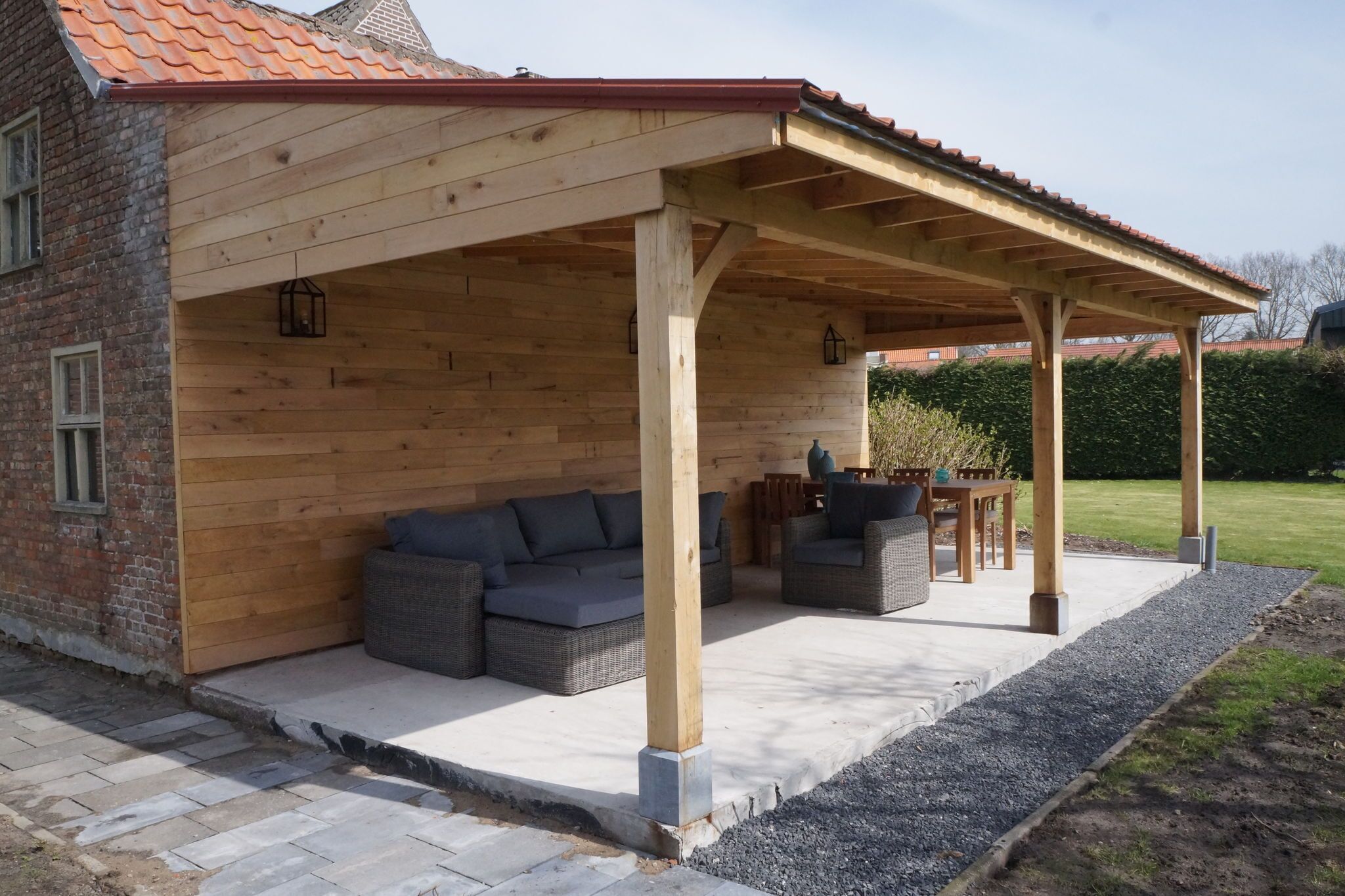 A covered outdoor seating area with a wooden structure, cushioned seating, and a table.