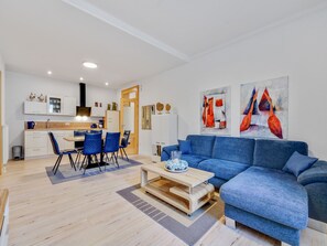 Een moderne woonkamer met een blauwe bank, een houten salontafel en een eethoek met blauwe stoelen.