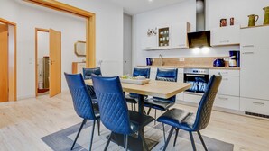 A modern kitchen with white cabinets, a built-in oven, and a microwave. There is a dining area with a wooden table and blue chairs. - Wohnung in Madfeld nahe Willingen Skilift (Brilon-Madfeld)