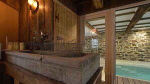 Un bassin en pierre avec une grille métallique, des murs en bois et un mur en pierre doté d’une porte en verre donnant accès à une piscine.