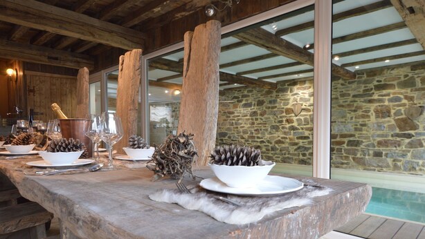 Une table en bois rustique, dressée pour un repas, avec un mur de pierres et une piscine en arrière-plan.