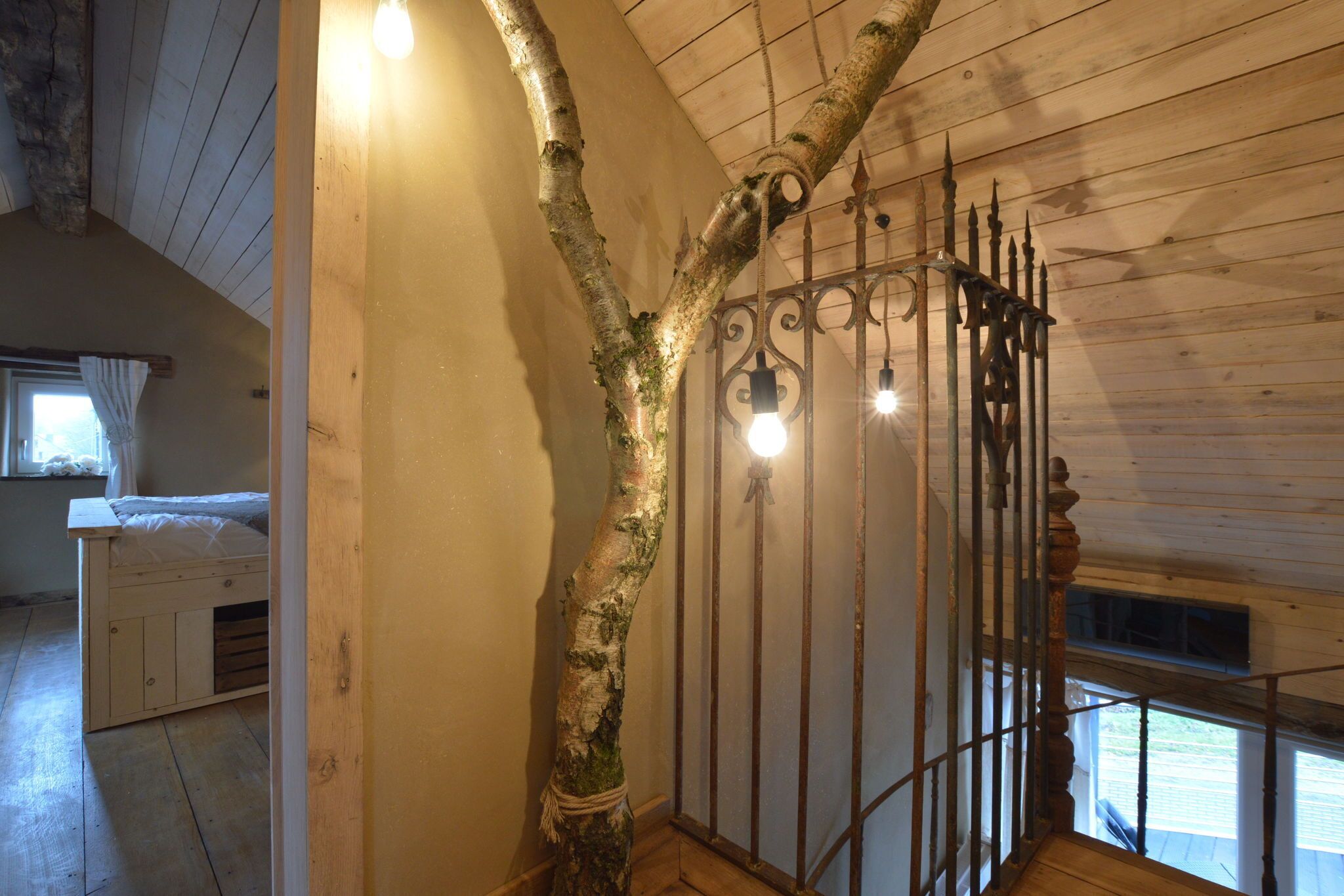 A rustic room with a wooden ceiling, a metal gate, and a bed with a white headboard.