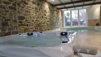 A hot tub with a stone wall backdrop, a glass door leading outside, and a towel and glass on the side.