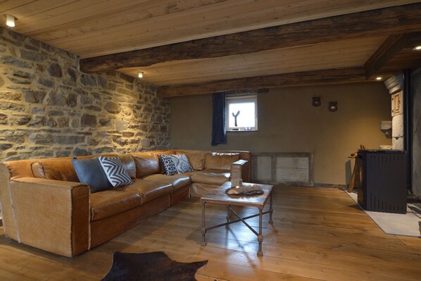 A rustic room with a stone wall, wooden ceiling, a leather sofa, a coffee table, and a fireplace.