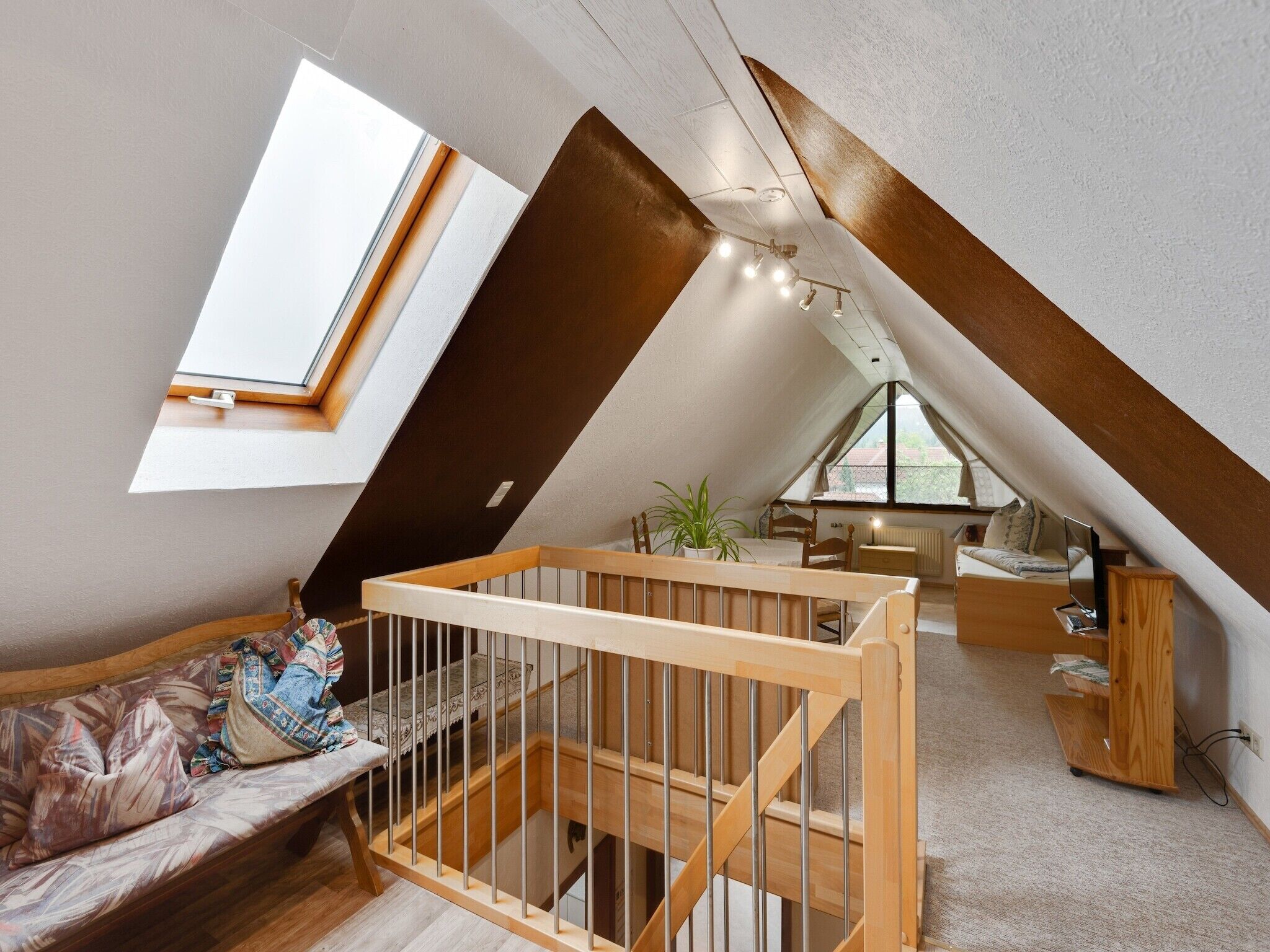 Un dormitorio acogedor en el ático con techo inclinado, una cama litera de madera, un escritorio pequeño y un ventanal que proporciona luz natural.
