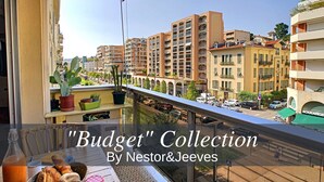 Un balcon donnant sur des immeubles de la ville, une table avec des aliments et une bouteille.