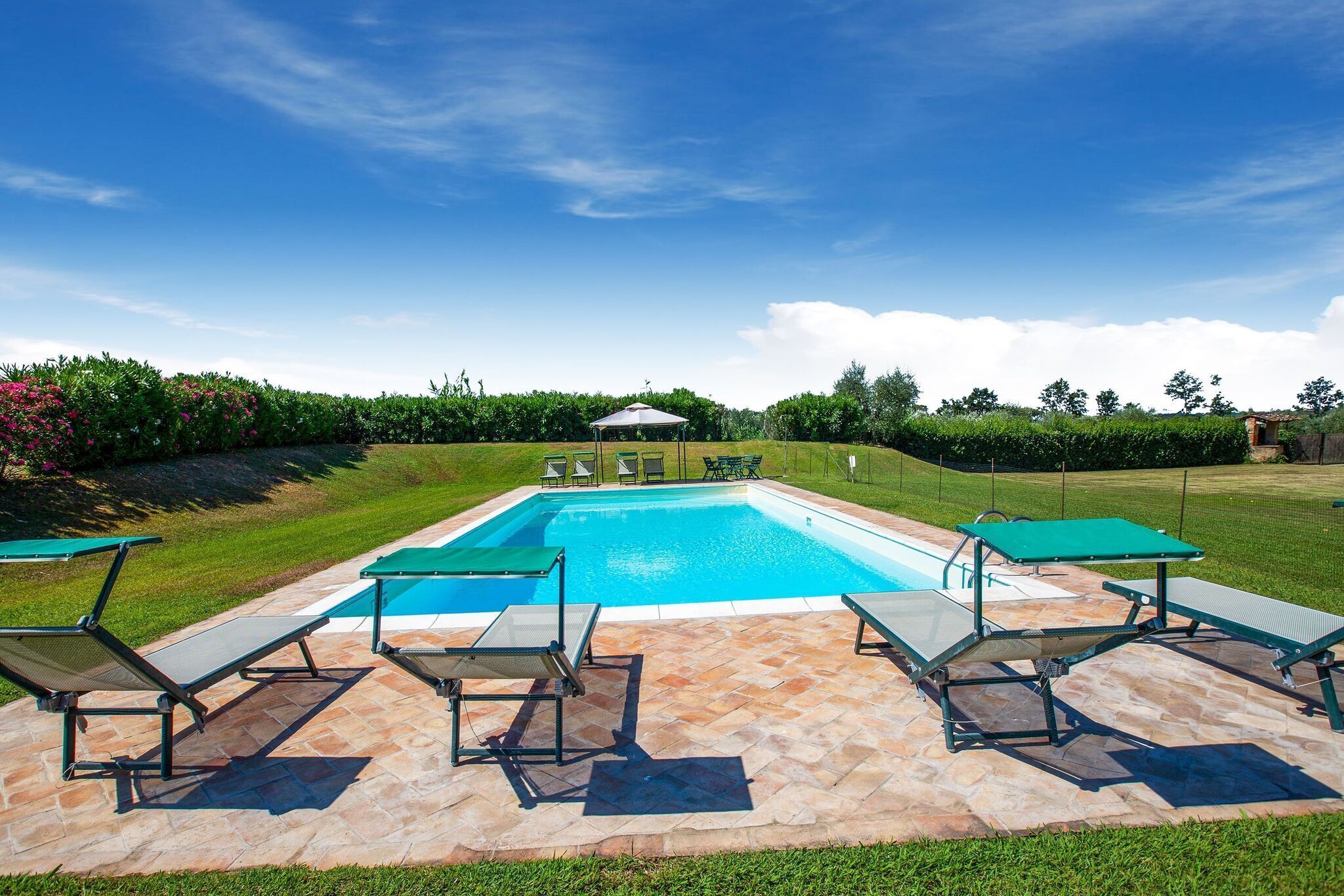 A rectangular swimming pool with a tiled deck, surrounded by lounge chairs and a covered seating area.