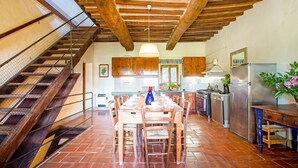Una cocina rústica con vigas de madera, una mesa de comedor para seis personas y una escalera con barandilla de metal.