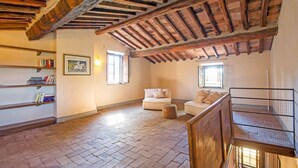 Una habitación rústica con vigas de madera a la vista, suelo de ladrillo, sofá, estantería y ventana.