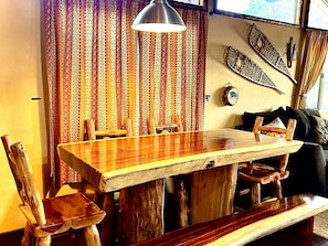 Un tavolo da pranzo in legno con sedie, una lampada a sospensione e una tenda decorata in una stanza accogliente.