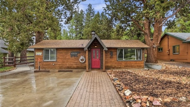 Une cabane en bois avec une porte rouge, un chemin bordé de briques et une bordure en pierres.