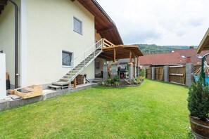 Uma casa de dois andares com varanda coberta, escadas e um pequeno jardim.