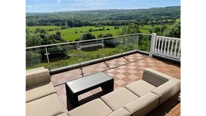 Un balcon doté d’un sol à carreaux, de sièges confortables et d’une rambarde en verre offrant une vue sur un paysage verdoyant.
