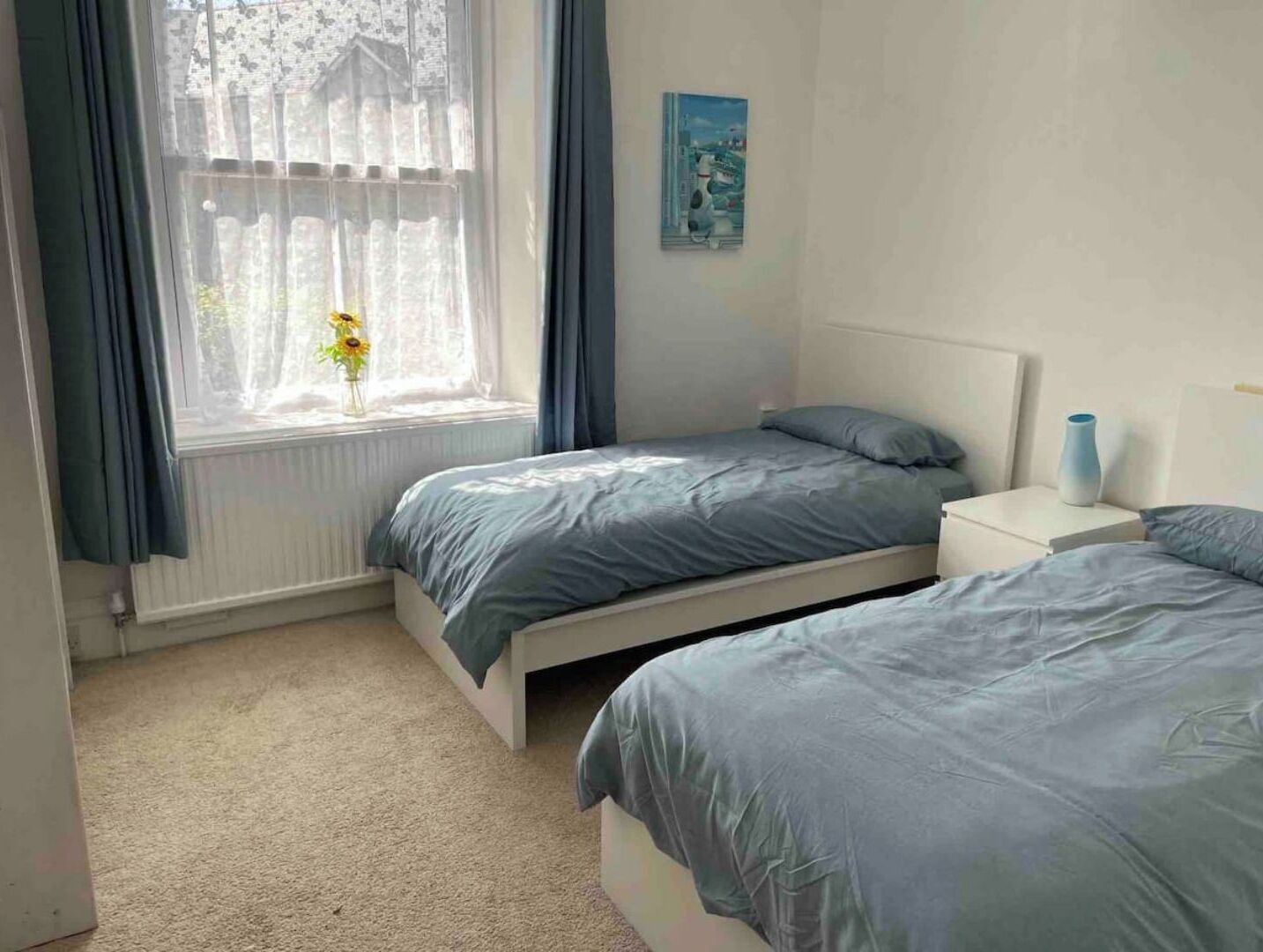 Un dormitorio con dos camas, una ventana con cortinas, un radiador y un cuadro en la pared.