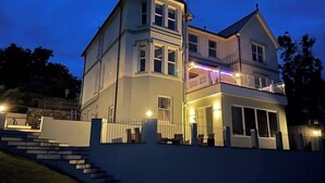 Une maison à deux étages dotée d’un balcon, d’un escalier menant à l’entrée et d’un éclairage extérieur soigné.