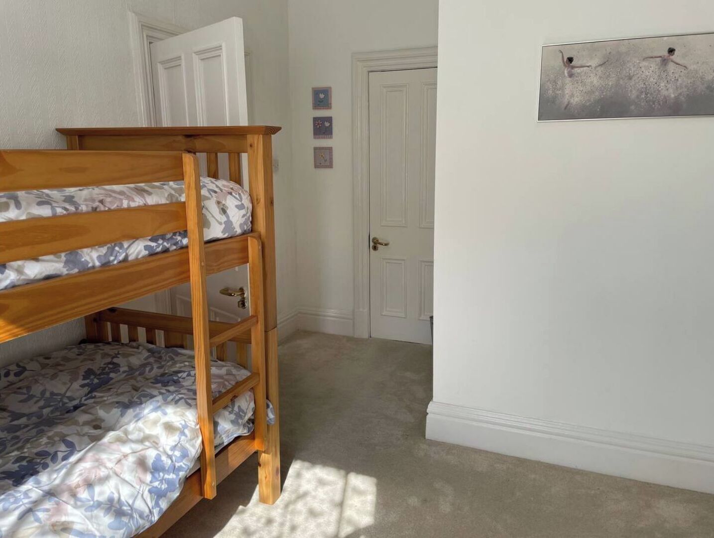 A bunk bed in a room with white walls, a door, and a framed picture on the wall.