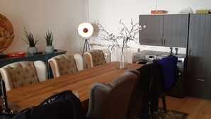 A dining area with a wooden table and chairs, a floor lamp, and a kitchen area with cabinets and appliances.