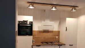 A compact kitchen with a built-in oven, a gas stove, and a sink. There are three pendant lights above the countertop.