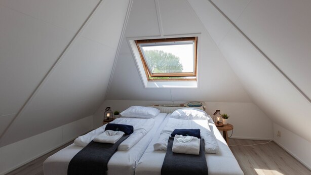 A bedroom with two beds, a skylight, a small table with a lamp, and a nightstand with a plant.