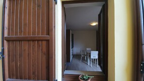 Una puerta de madera con mecanismo deslizante, una planta en maceta en el umbral y una vista de una habitación con una mesa y sillas para comer.