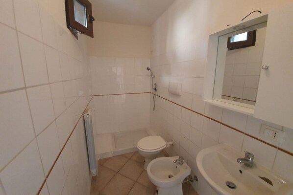 Un baño pequeño y limpio con azulejos blancos, inodoro, bidé, lavamanos y espejo.