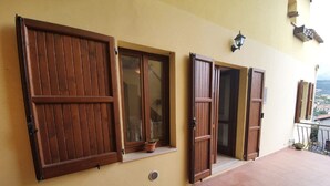 Un edificio con grandes contraventanas de madera, un pequeño ventanal con una planta en maceta y un balcón con vistas al paisaje.