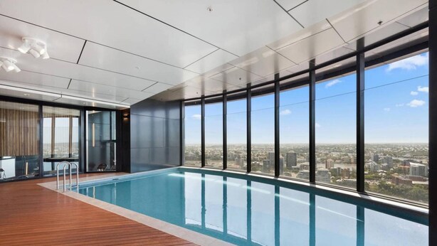 A modern indoor swimming pool with a city view, wooden deck, and large windows. - 2BR Luxury Skytower CBD Pool Gym Netflix (Brisbane)